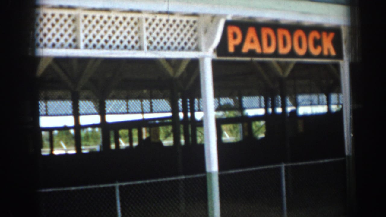 Covered paddock entrance with orange PADDOCK sign and chain-link fence.