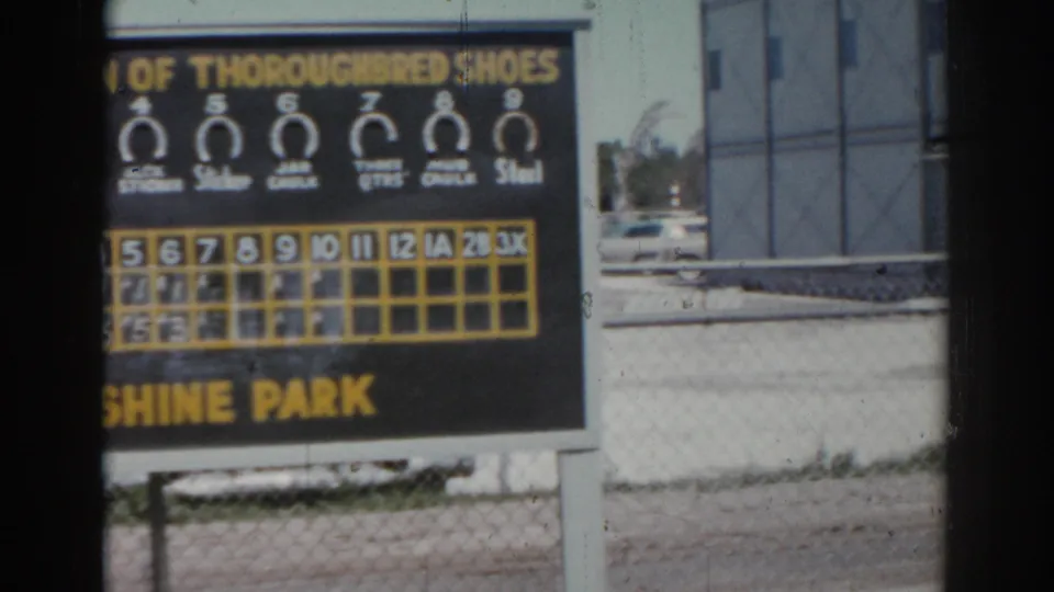 The pan moves across part of the Sunshine Park scoreboard, leaving the result grid and lower sign visible near the fence.