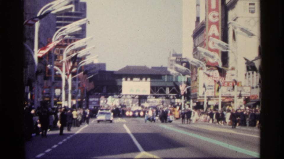 A busy street with a vertical CHICAGO sign in a home movie